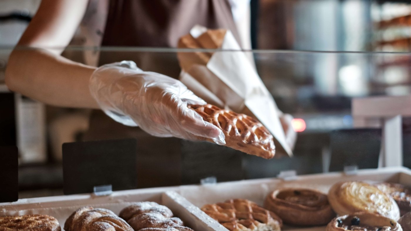 European woman sells in bakery putting bread in paper bag.