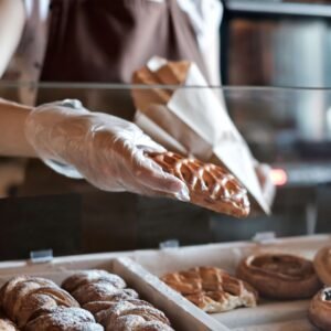 European woman sells in bakery putting bread in paper bag.